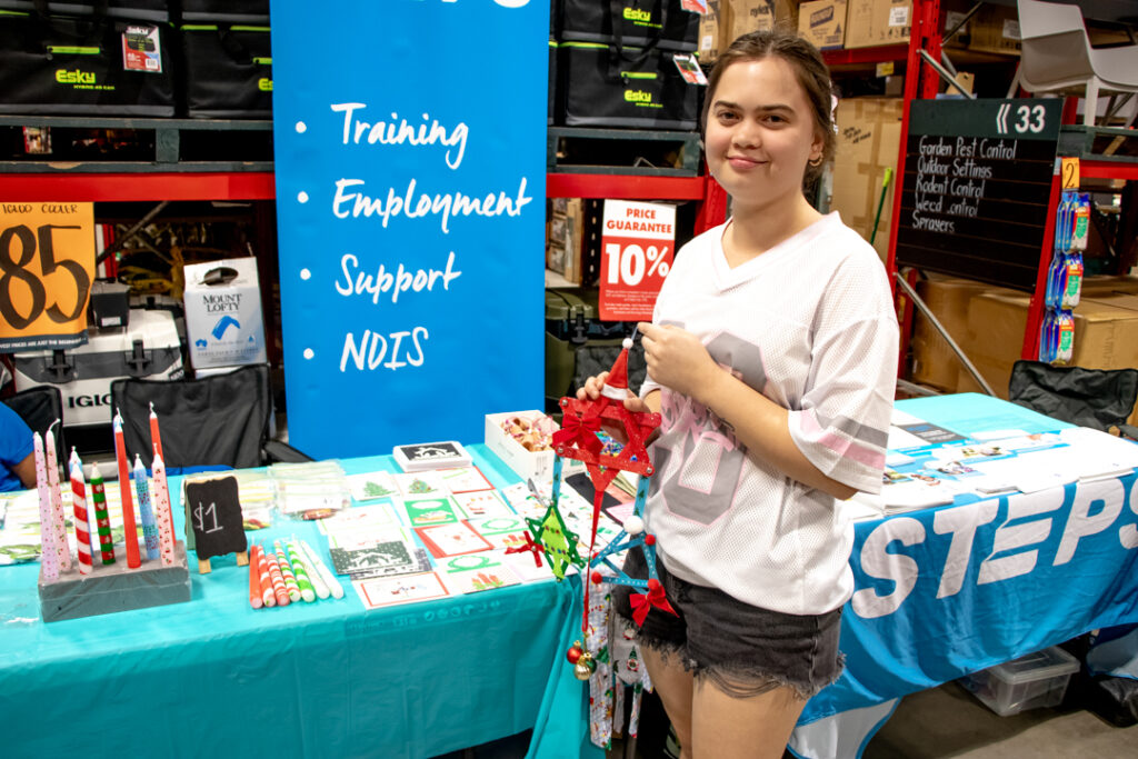 STEPS participant holding a handmade decoration in front of two tables.
