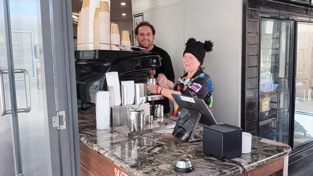 A man and woman stand behind a café counter, smiling.