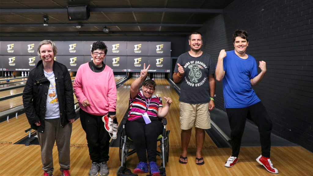 Five STEPS Community Support participants having fun at a bowling alley, posing and smiling at the camera.