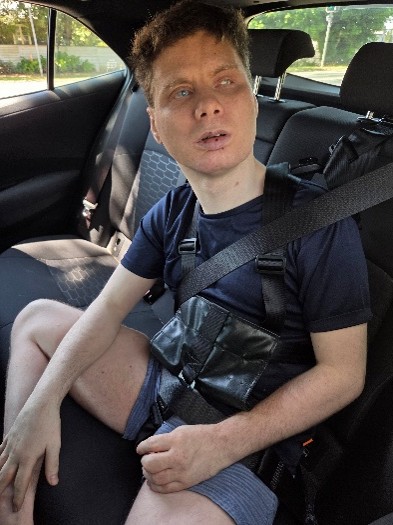 STEPS Community Support participant David sits in the backseat of a car. He is a young man, looking off-camera out the car window.