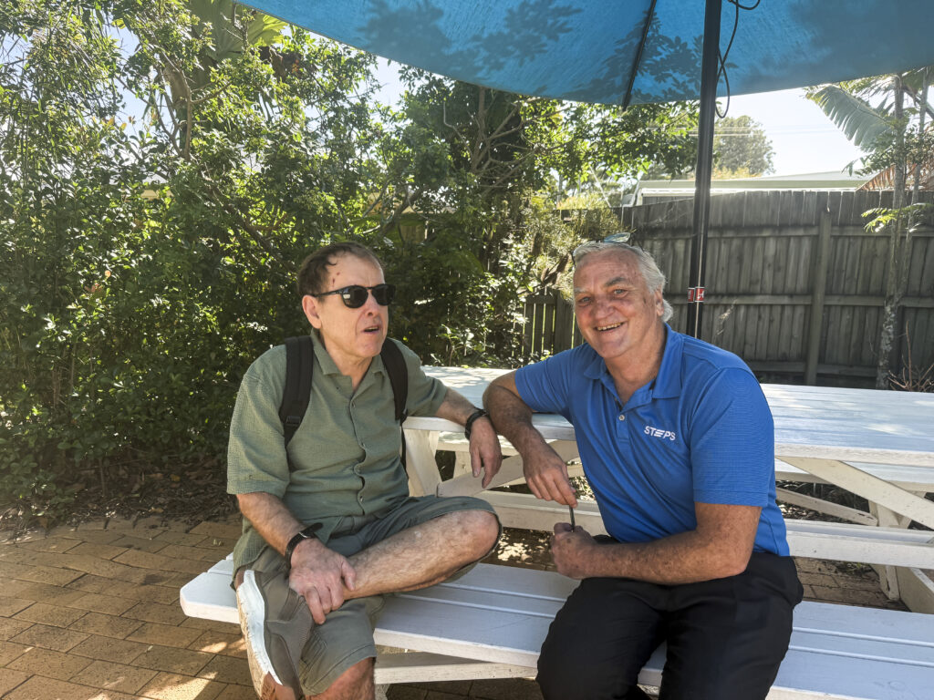 STEPS Positive Behaviour Support client and trainer sit together on white bench.
