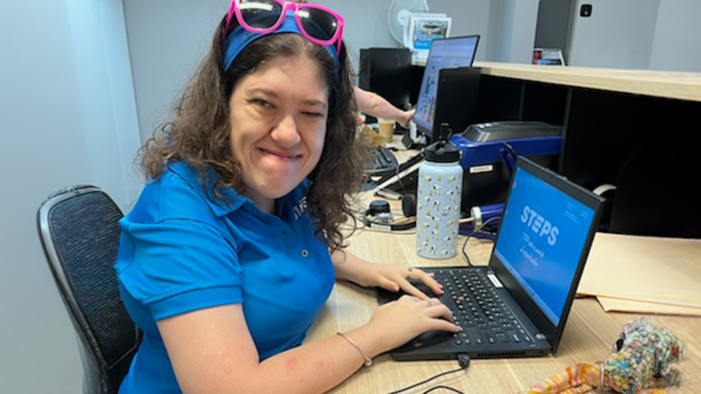 Imogen sitting at the desk in a classroom, with a laptop open in front of her with a blue STEPS wallpaper.