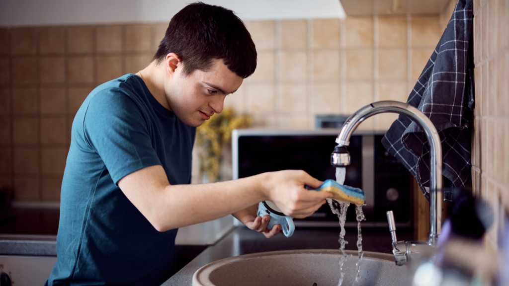 Person washing a dish at a kitchen sink, illustrating everyday living supported through Individualised Living Options.
