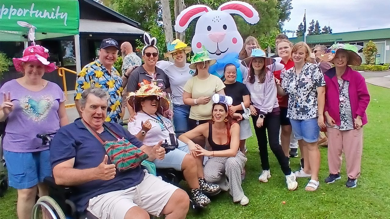 A crowd of people dressed colourfully, standing on a bright green lawn. Someone is dressed as the Easter Bunny.