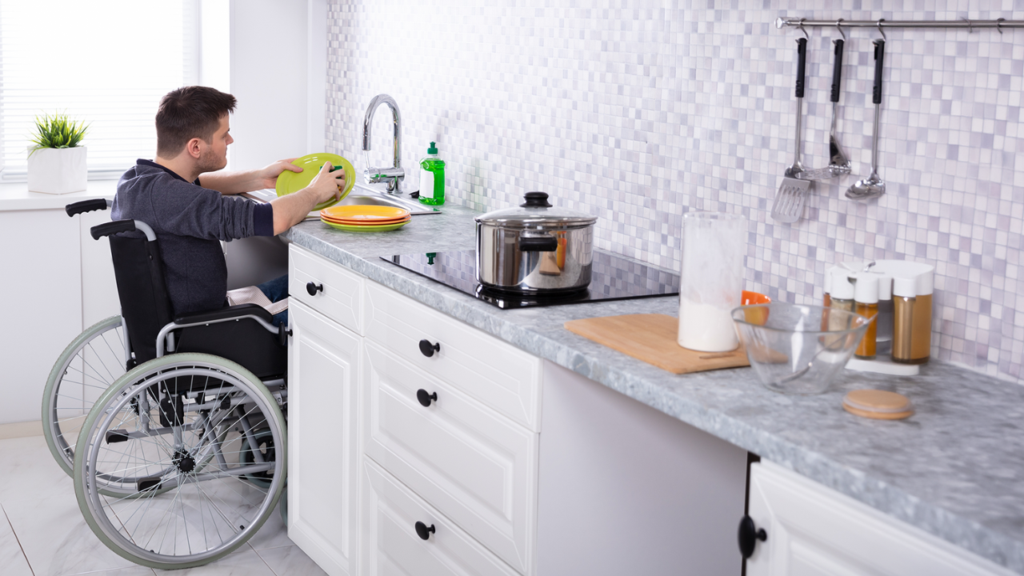 Person using a wheelchair washing dishes at a kitchen sink, illustrating everyday living supported through Individualised Living Options.