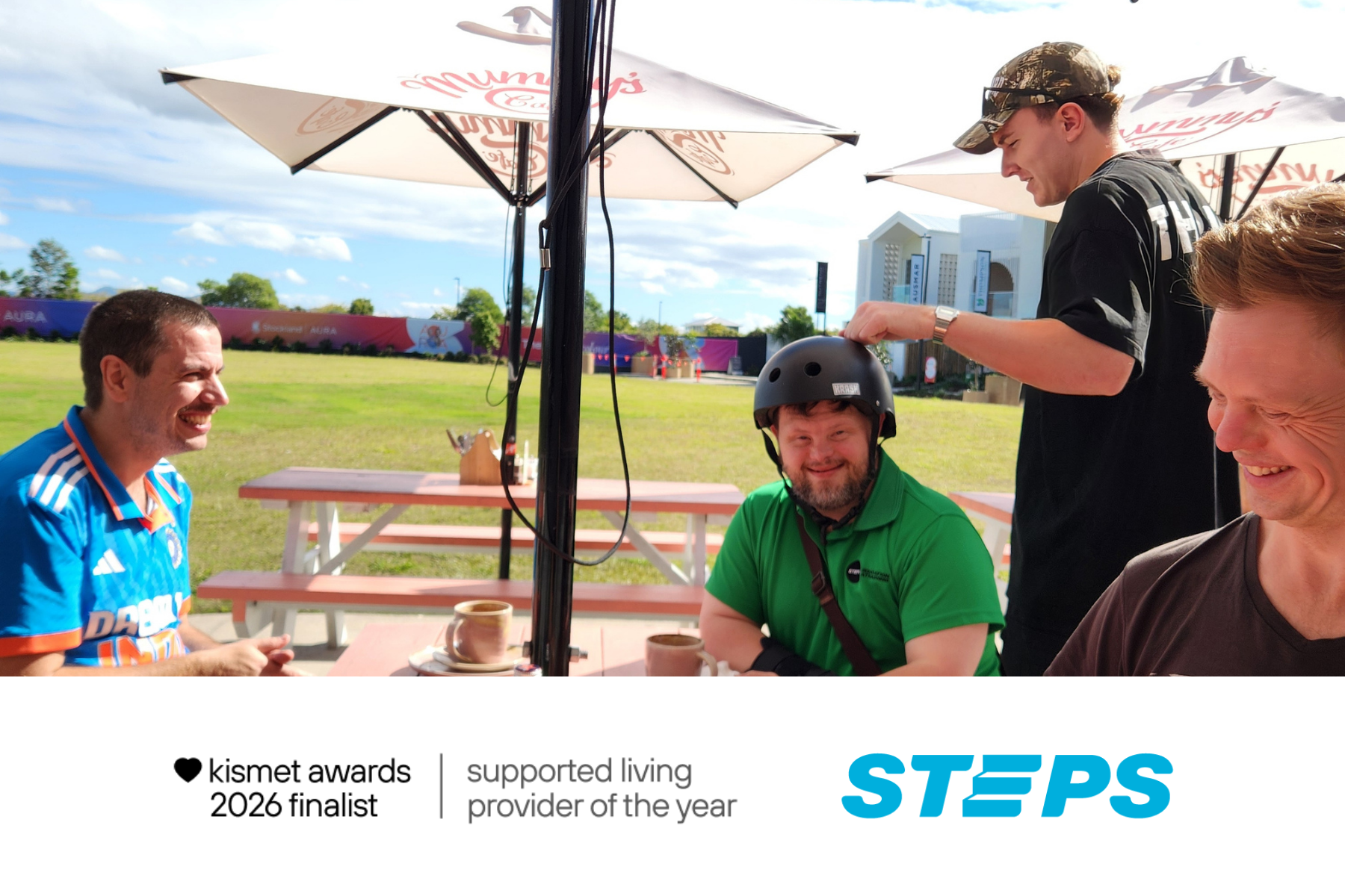 Four men sitting at table outside a cafe near a field. Text in white rectangle reads: Kismet awards 2026 finalist | supported living provider of the year.