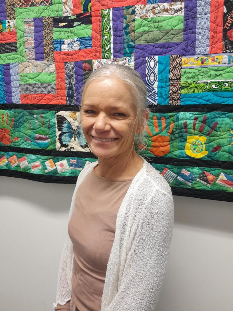 STEPS SEE participant standing in front of a handmade quilt.