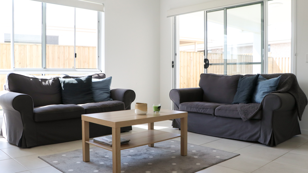 Two black couches and a coffee table in a white pristine living room on a bright day.