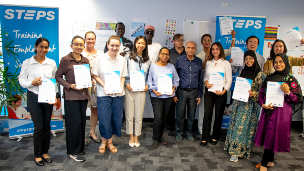 Several STEPS AMEP Ready for Work clients stand in a classroom in Darwin, proudly holding their graduation certificates and smiling at the camera.