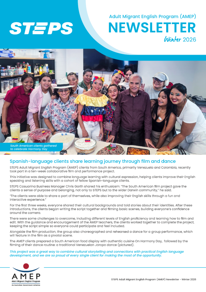 Group of Adult Migrant English Program clients gathered around a table of South American dishes, celebrating Harmony Day in a classroom setting.