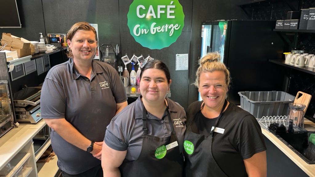 Three STEPS Cafe on George team members standing behind Cafe counter, smiling at camera.
