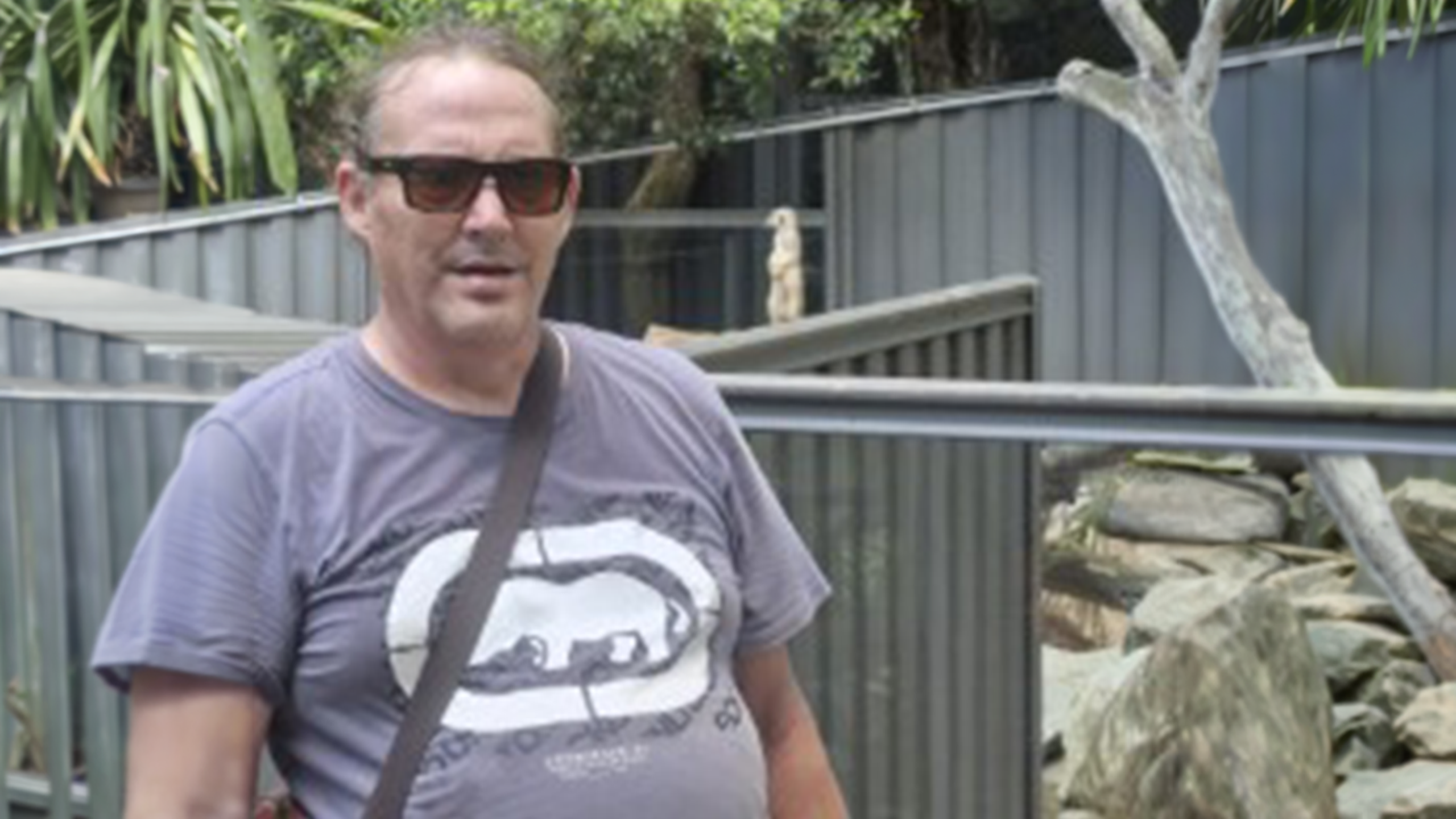 Four people are in a public undercover swimming pool, waving and smiling at camera.