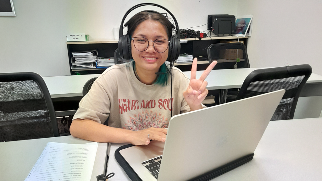 Somalisa wearing headphones and smiling while working on a laptop during a STEPS Skills for Education and Employment class.