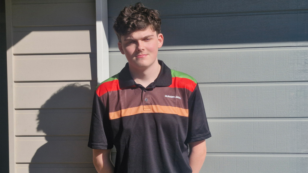 A young man wearing a Hungry Jack's uniform, looking at the camera, hands respectfully behind his back.