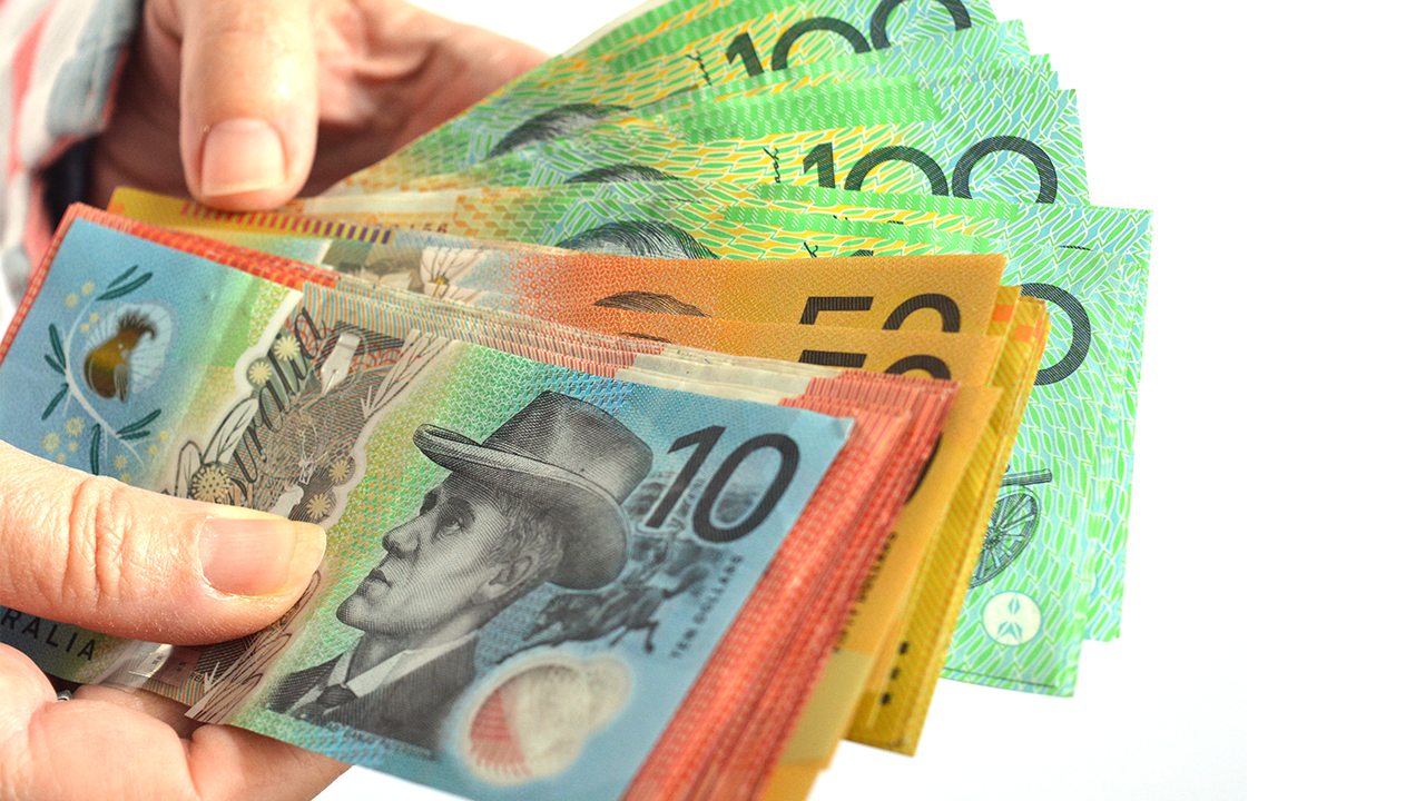 A hand holding a fanned-out stack of Australian banknotes, including $10, $20, $50, and $100 notes.
