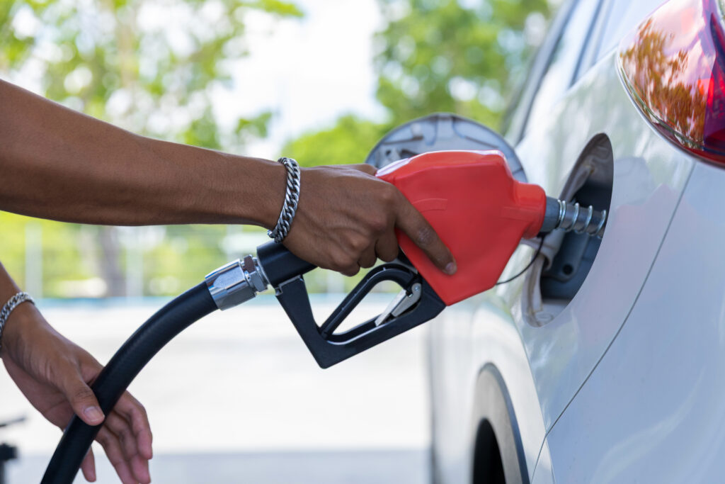A person refuelling a white car with a fuel pump nozzle.